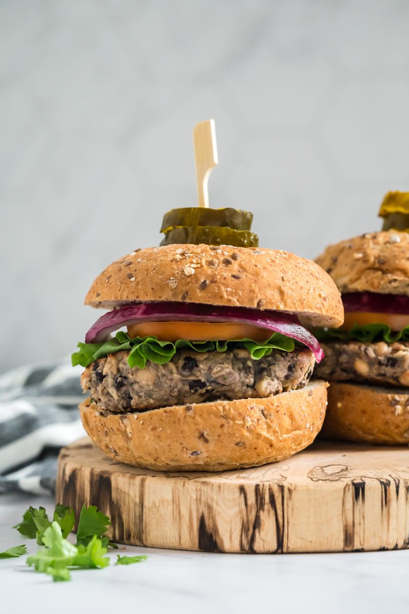 Vegetarian bean burgers with black and white beans served on a whole wheat bun with lettuce, tomatoes, red onion, and pickles.